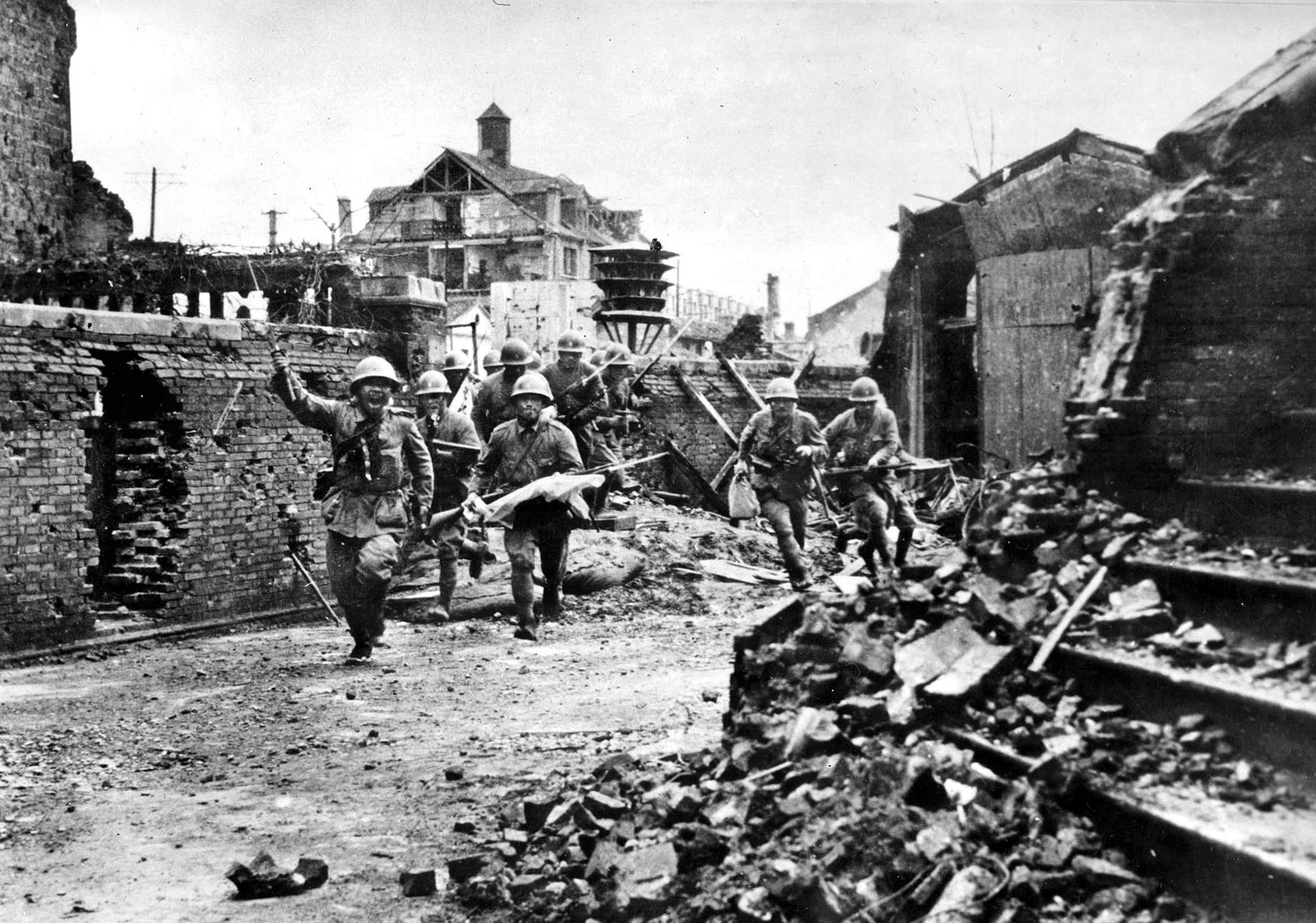 Japanese soldiers rapidly advance through a rubble-strewn street in the city of Toh-an, China. Locked in close combat with Chinese troops, the Japanese pushed toward Kiukang, the terminus of the Nan-Hsun Railway.