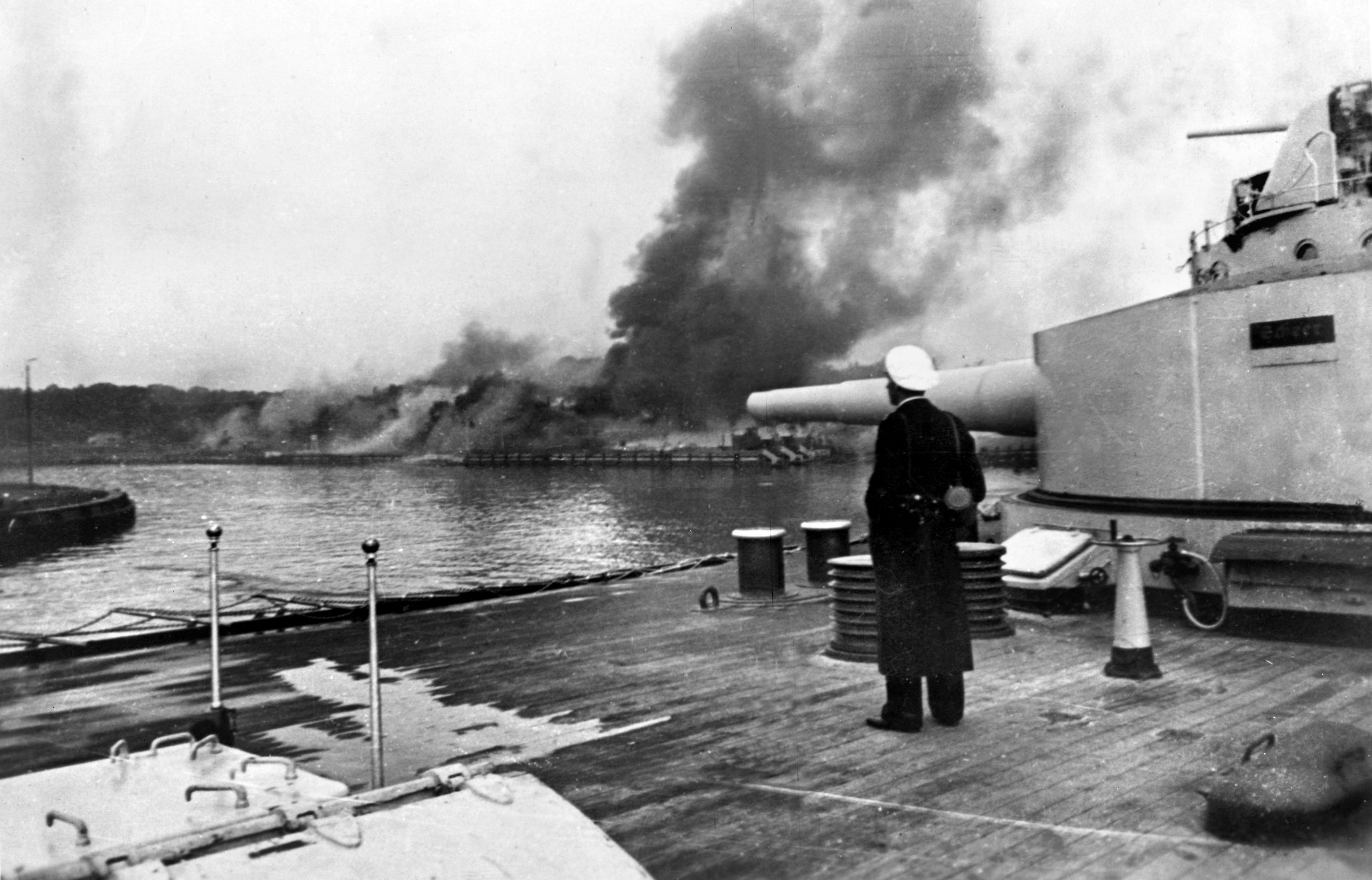 While a German naval officer stands on deck, the guns of the old battleship Schleswig-Holstein fire on the Polish ammunition depot on the Westerplatte near the free city of Danzig during the opening hours of World War II, September 1, 1939.