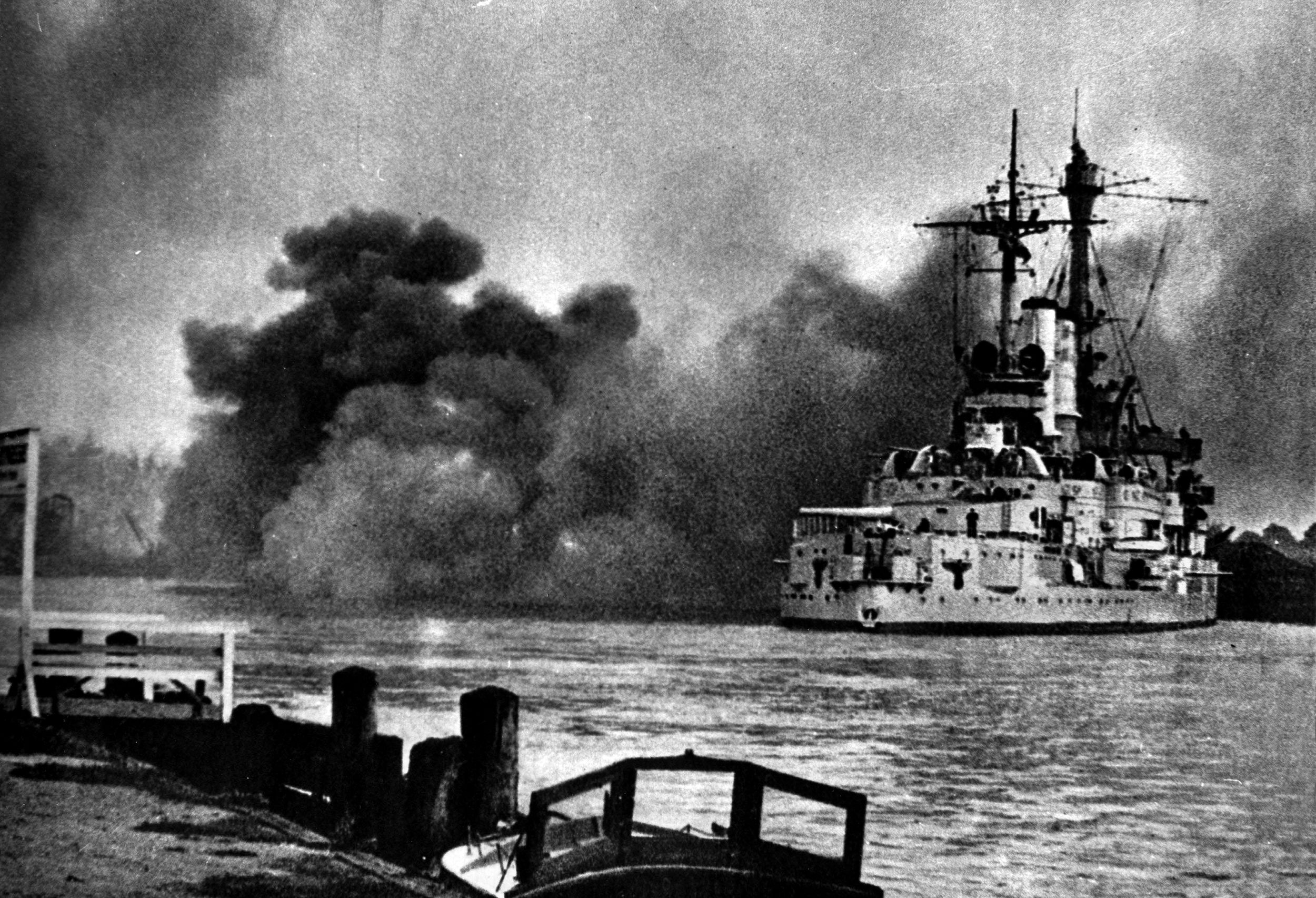 The big guns aboard the battleship Schleswig-Holstein fire away at the Poles ensconced at the Westerplatte. Feigning a goodwill visit, the Germans sent the old battleship, with combat troops secretly aboard below decks, to an advantageous position before the outbreak of World War II.