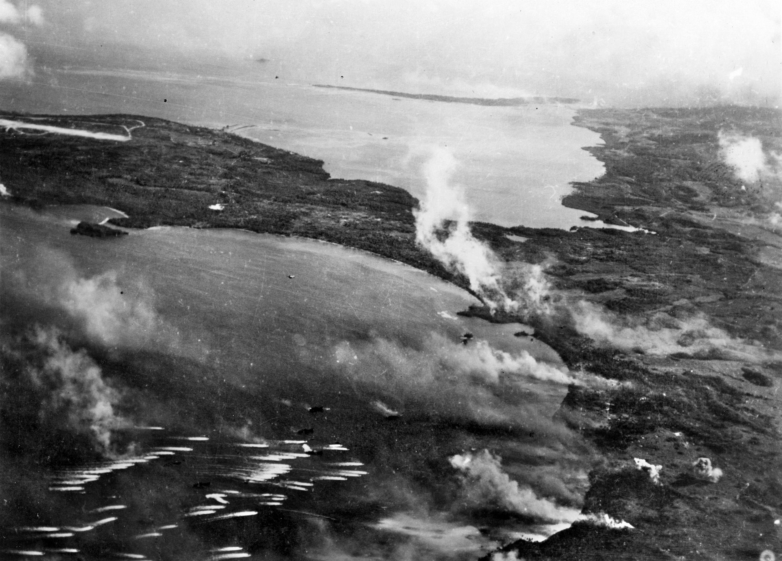 American landing craft leave white wakes as they make their runs toward the landing beaches on Guam. Smoke from the pre-invasion bombardment drifts toward them during their approach.