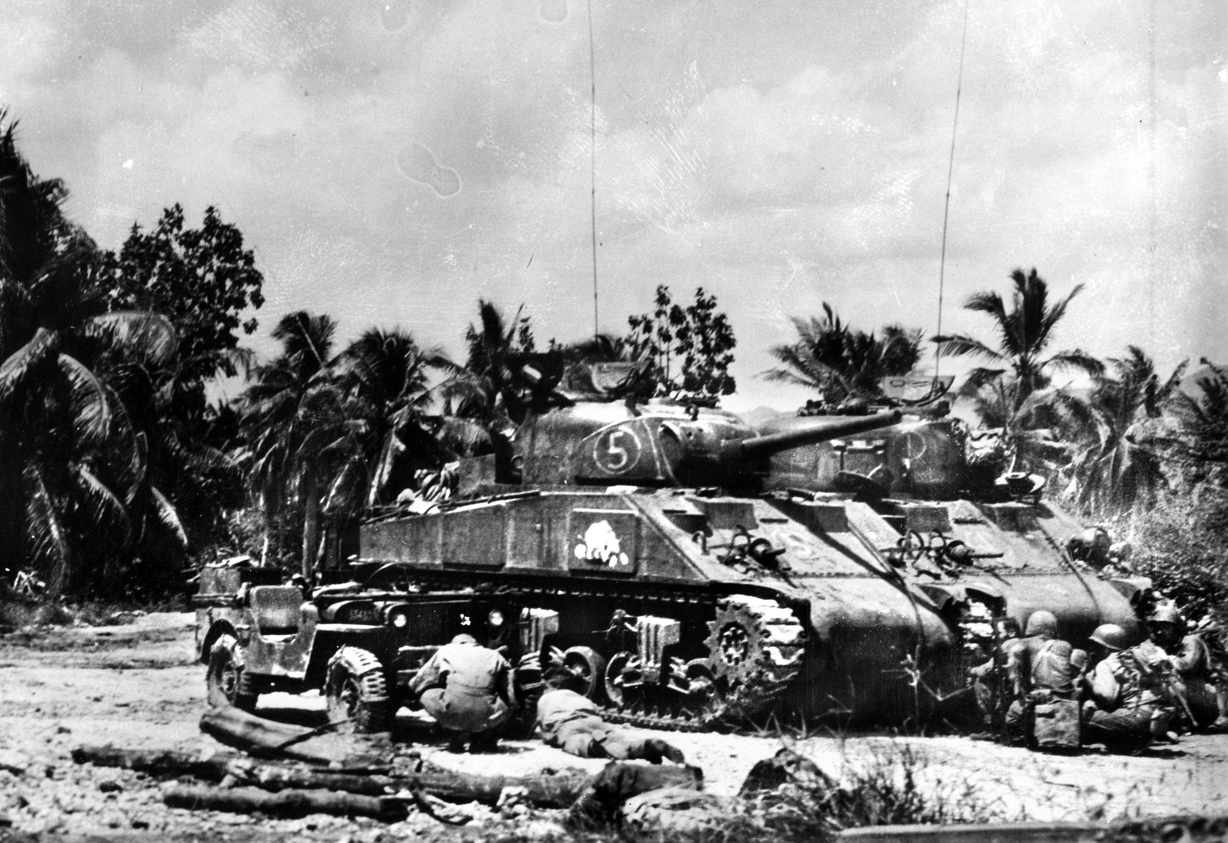 Suddenly caught in a Japanese crossfire, Marines take cover behind an M4 Sherman medium tank and a Jeep during their advance on Guam.