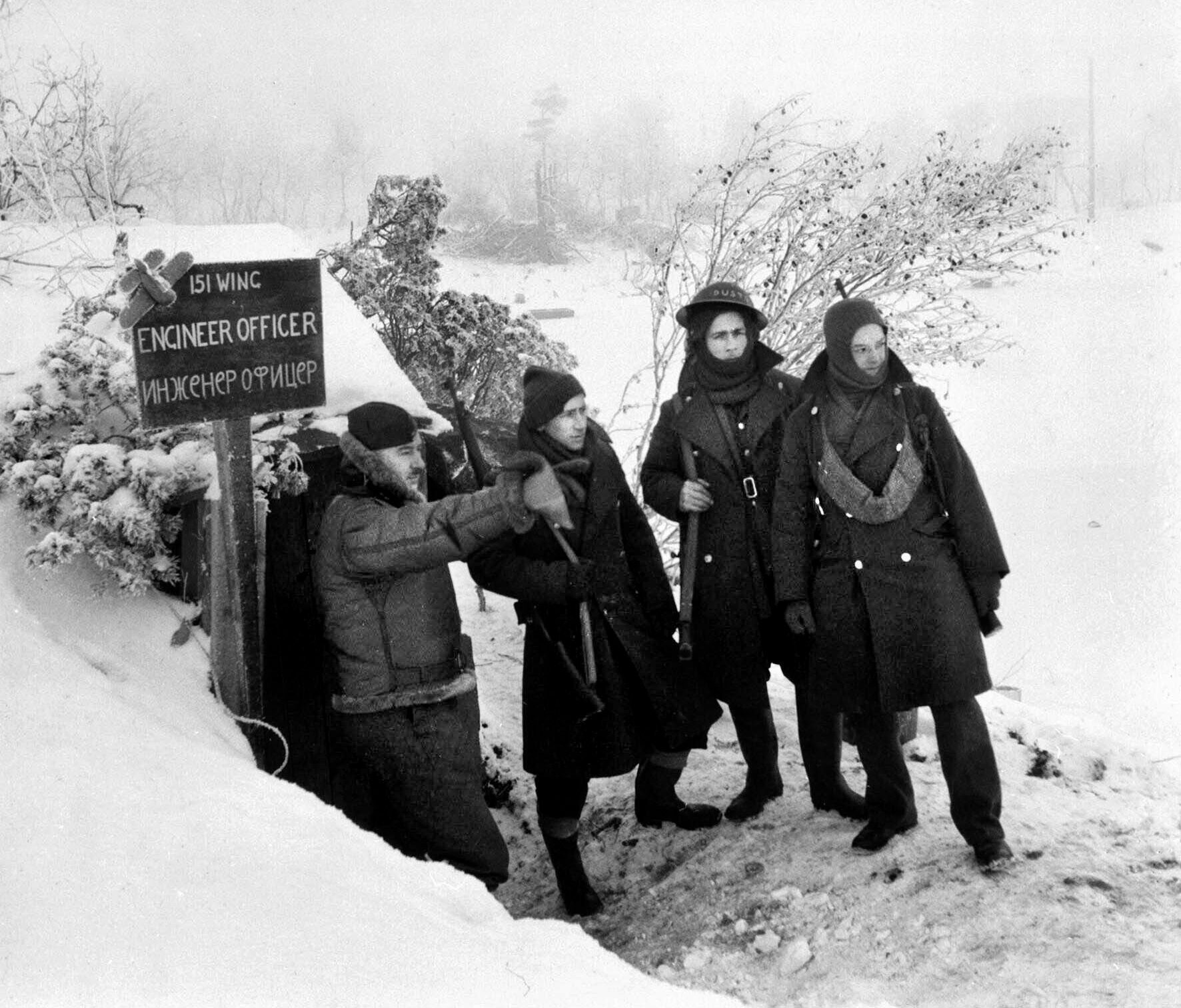 As temperatures in Russia plunge to -15 degrees Fahrenheit in October 1941, Flight Engineer Gittins of No. 151 Wing RAF talks with sentries at a snow covered airfield.