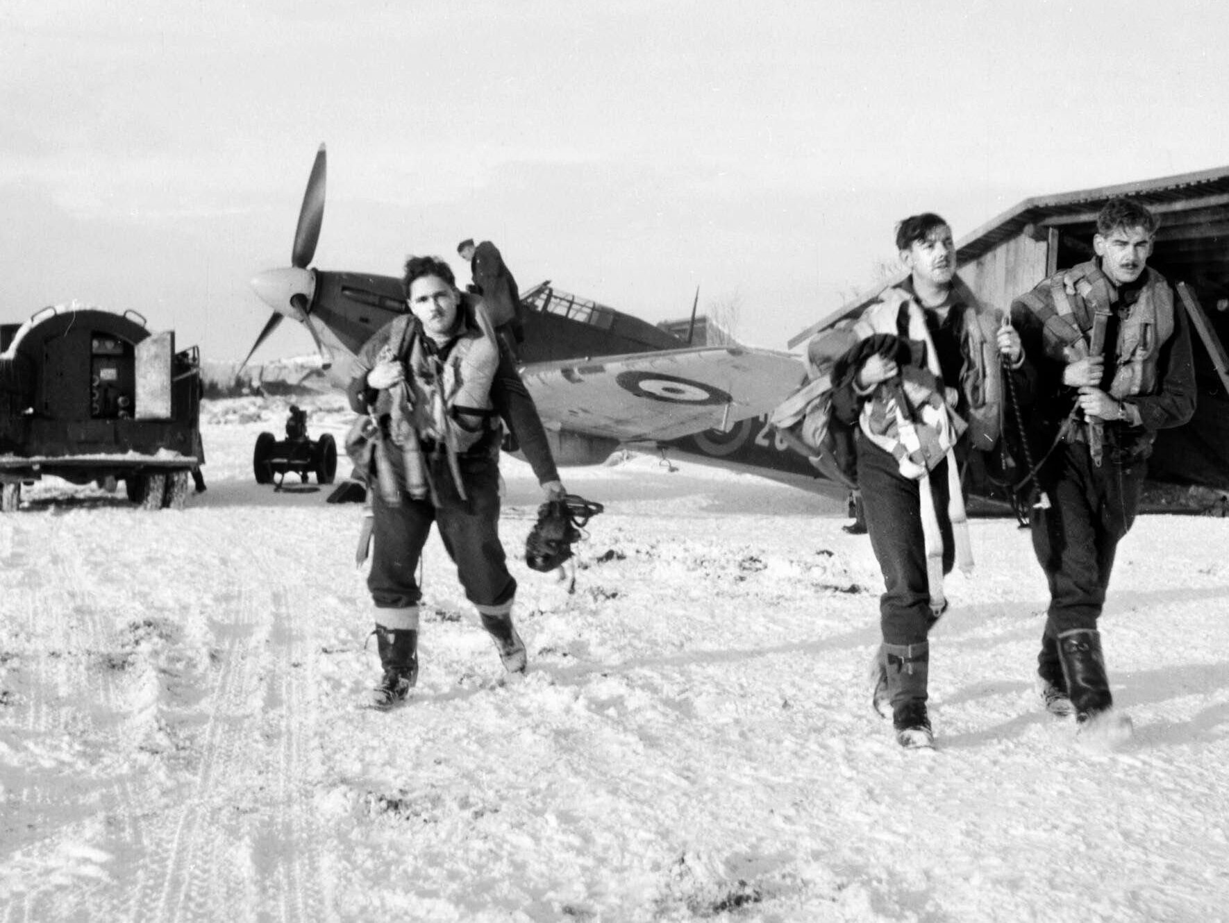 As a Hurricane fighter is refueled in the background, RAF pilots of No. 134 Squadron head for a debriefing by their intelligence officer after escorting Soviet bombers on a mission over areas of Russia occupied by German forces.