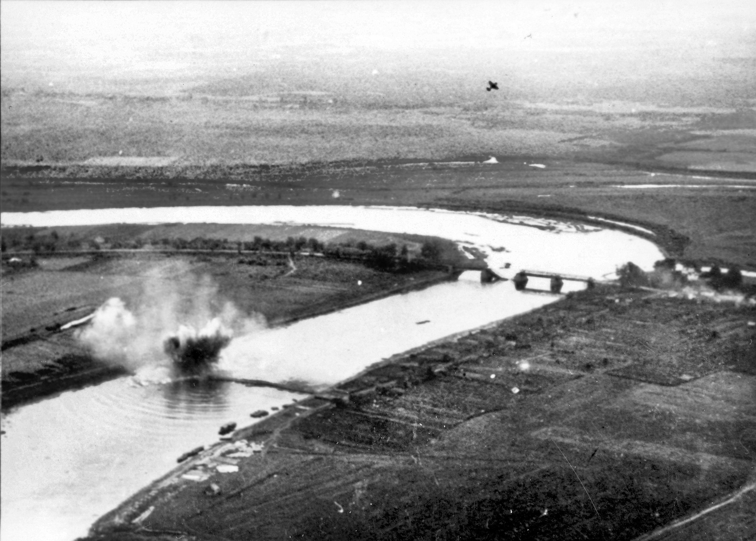 High above the previously destroyed concrete bridge, a Junkers Ju-87 “Stuka” from Sturzkampfgeschwader 2 (Dive Bomber Wing 2) can be seen climbing after an apparently successful attack on a Soviet pontoon bridge across the Volkhov River in Russia, August 1941.
