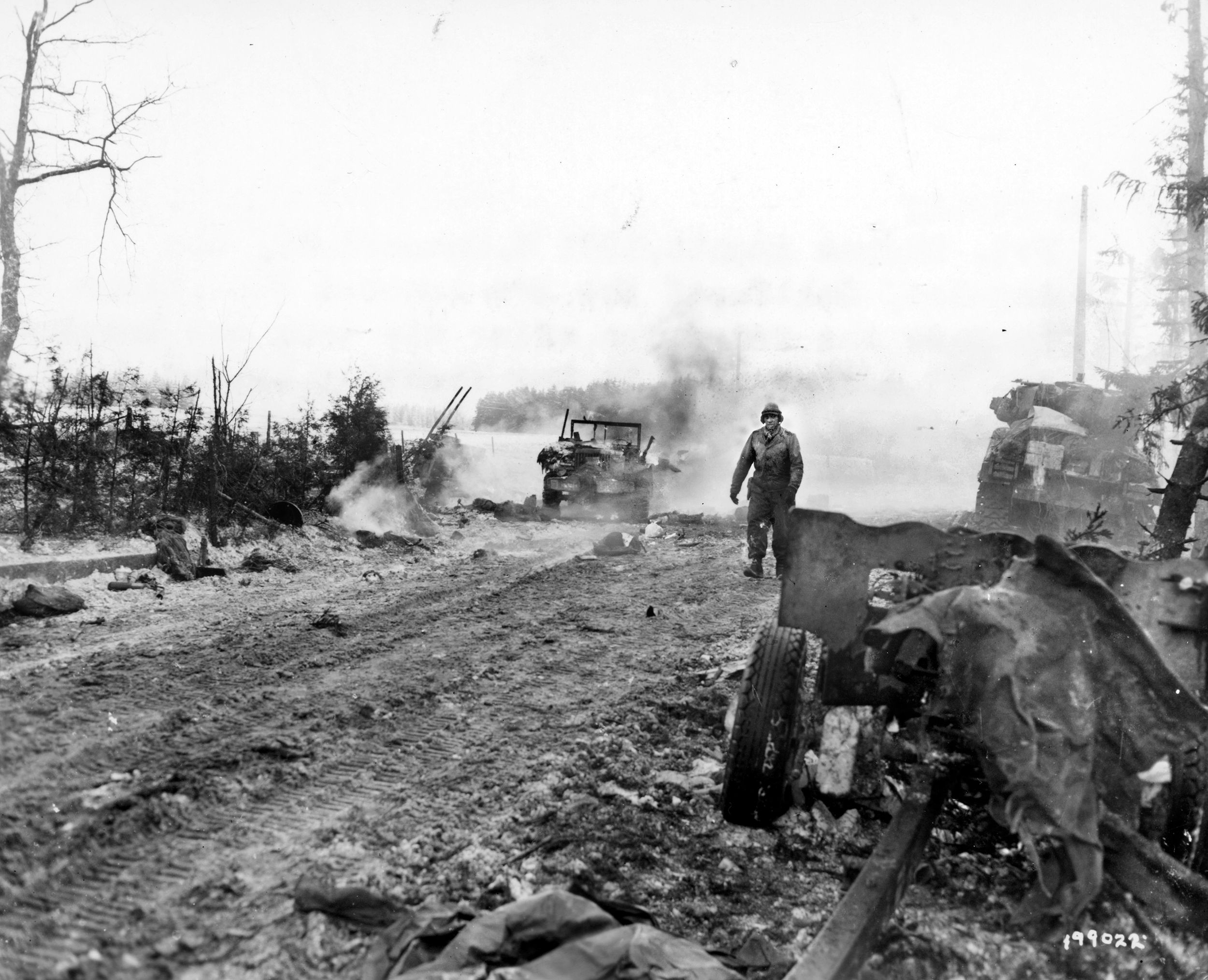 With the smoke of battle all around, Private Thomas Amenta hikes back to the rear area after his tank was knocked out by a road mine in the fighting beyond Langlire, Belgium, during the First Army drive into the Ardennes salient on January 11, 1945. Obstacles faced by newly promoted Major George Stallings Jr. and Company D (2nd Battalion, 33rd Armored Regiment) as they pushed into Belgium and, eventually, Germany, included ice, snow, mines, knocked out bridges and, occasionally, no roads at all.