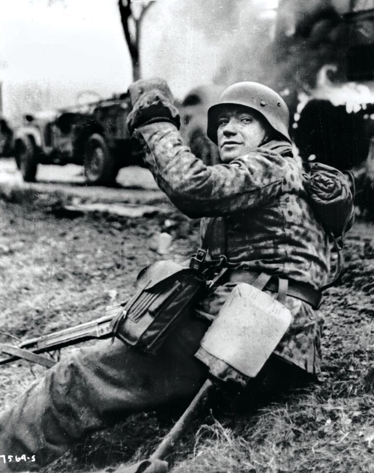This captured German film shows  a grenadier of Kampfgruppe Hansen posing in front of burning vehicles of the U.S. 14th Mechanized Cavalry Group during the Battle of the Bulge.