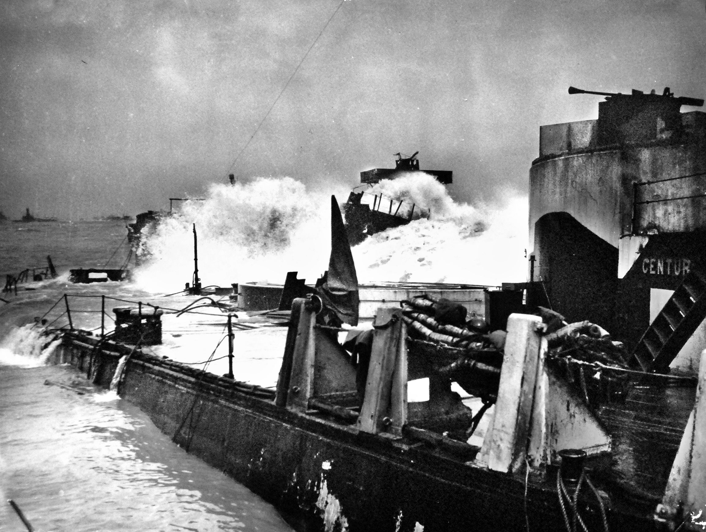 This image from a Coast Guard LCI (L) in June 1944, shows a wave from the worst storm to hit the French coast in 40 years battering the line of 23 freighters scuttled by the Coast Guard to form a breakwater known as a “Gooseberry” to protect the artificial Mulberry harbor, drastically reducing the toll of destruction and ensuring the flow of supplies to the front. 