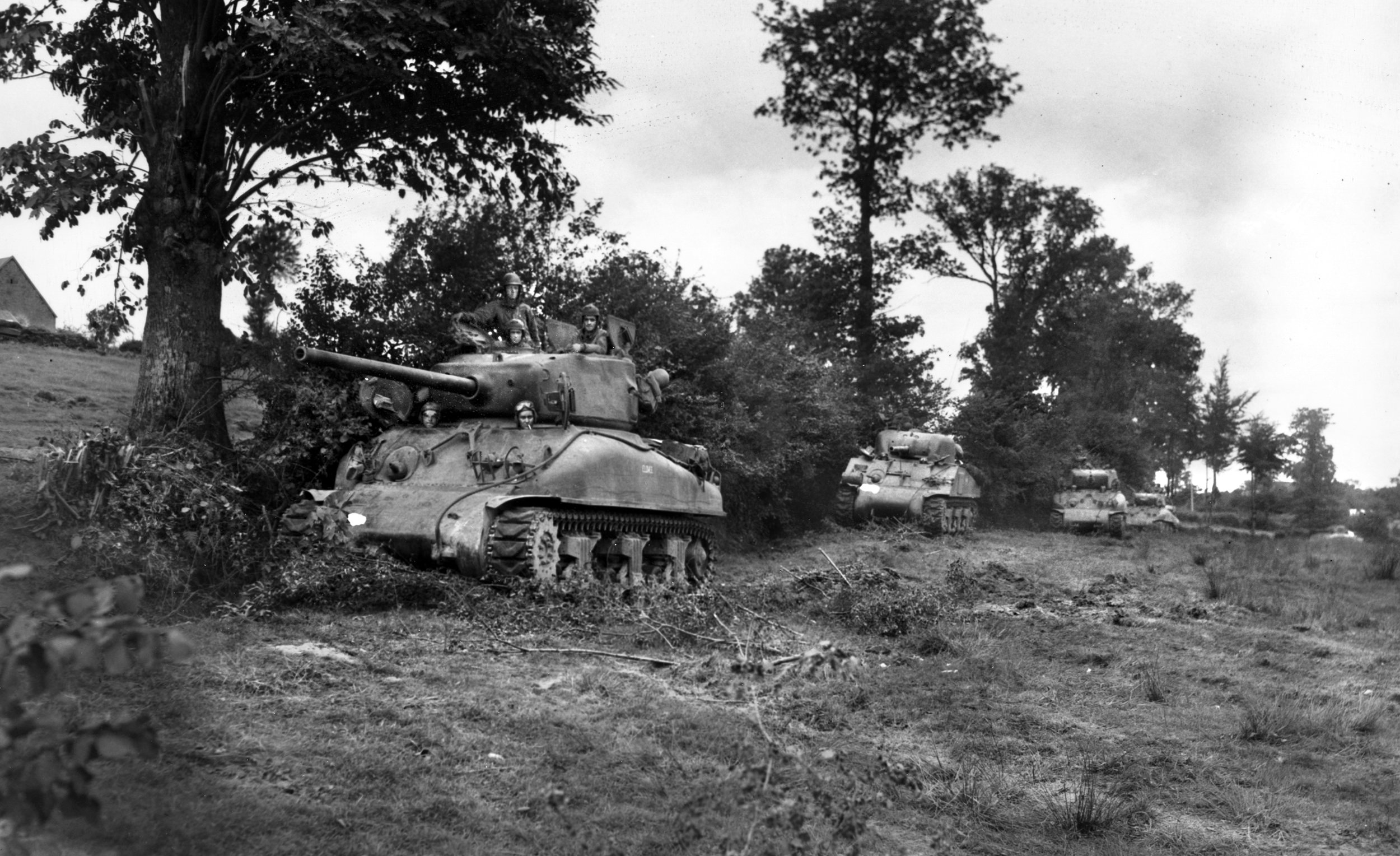 American Sherman tanks use a hedgerow as cover in Normandy in the summer of 1944. After failing to take Hill 192 in June, the men of the 2nd Division trained with the 741st Tank Battalion to coordinate another attack on July 11. Assisted by a rolling artillery barrage, the attack was successful, though costly, with some 3,000 wounded and nearly 600 dead.