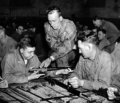 Staff Sgt. Junior Spurrier (left) demonstrates the disassembling and cleaning of an infantry weapon in a promotional photo.