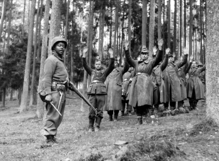 A 12th Armored Division GI stands guard over a group of surrendering Wehrmacht soldiers in April 1945. Manpower shortages forced the U.S. Army to retrain soldiers in service units—including African-Americans—as combat riflemen in 1945.