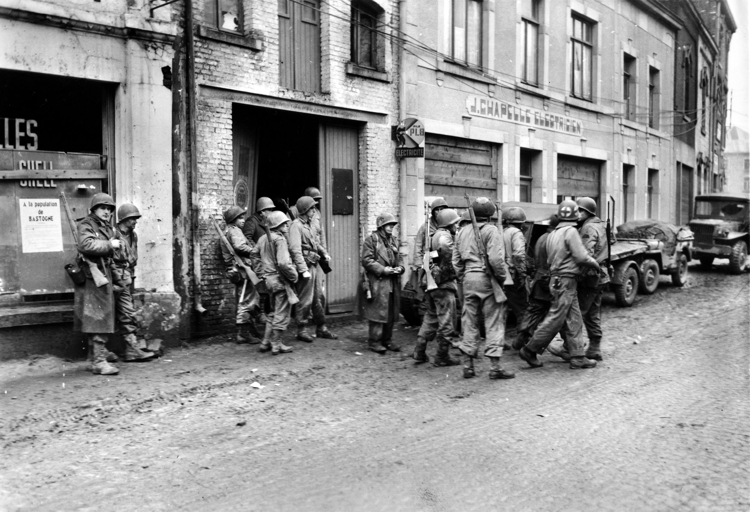 Battle-weary survivors of the 28th Infantry Division gather in Bastogne after narrowly escaping the German “Watch on the Rhine” offensive. While the division bore the brunt of the initial surprise attack, the cost of their stand was devastating. From the fierce defense at Hosingen, Luxembourg, only a small remnant of the original garrison managed to evade capture—some 300 GIs were taken prisoner—and navigate through enemy-territory to rejoin Allied lines.