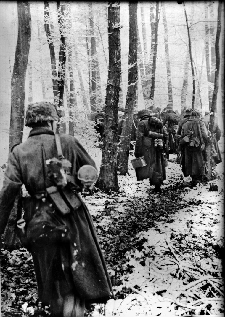 Members of a Volksgrenadier division (VGD) in the opening hours of the Ardennes Offensive, December 16, 1944. The Germans used the rugged Luxembourg forest to try to bypass the American strong points in the overstretched Allied “Ghost Front.” After losing close to a million men fighting in Normandy and Russia in the summer, Germany was forced to create VGDs mixing seasoned veterans and fresh recruits armed with submachine guns (like the MP40 or the newer StG 44) to compensate for their smaller size.  