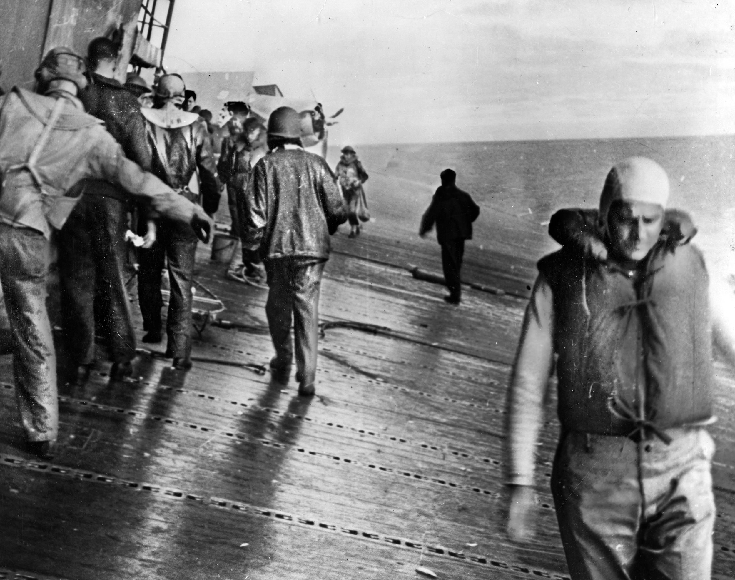 The deck of the carrier USS Yorktown lists sharply after it was struck by two Japanese aerial torpedoes on June 4, 1942. Looking aft from alongside the island as men prepare to abandon ship, Fighting Squadron Three’s F4F-4 Wildcat (Plane #6) is visible. Ensign Brainard T. Macomber had flown it during the morning strikes on the Japanese carriers, but it could not be sent back aloft to intercept the afternoon torpedo bombers that ultimately crippled the carrier due to insufficient fuel.