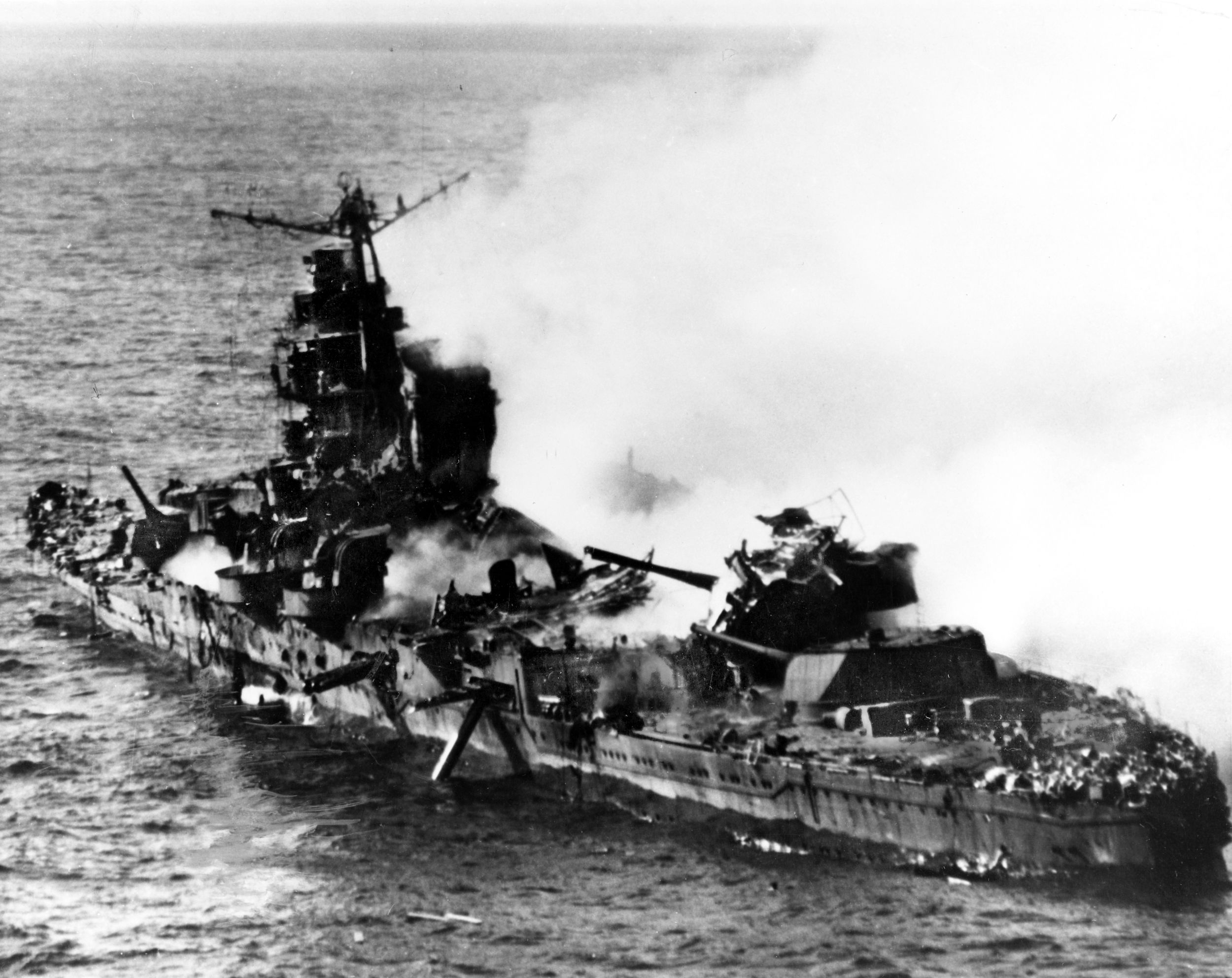 The Japanese heavy cruiser Mikuma wallows in the Pacific during the afternoon of June 6, 1942, after devastat- ing attacks by dive-bombers from the USS Enterprise and USS Hornet during the final stages of the Battle of Midway. Taken from a scouting Enterprise SBD Dauntless, this photo highlights the catastrophic damage inflicted on the vessel—shattered midship structure, a torpedo dangling from the aft port-side tubes, and heavy wreckage on top of her number four eight-inch gun turret.