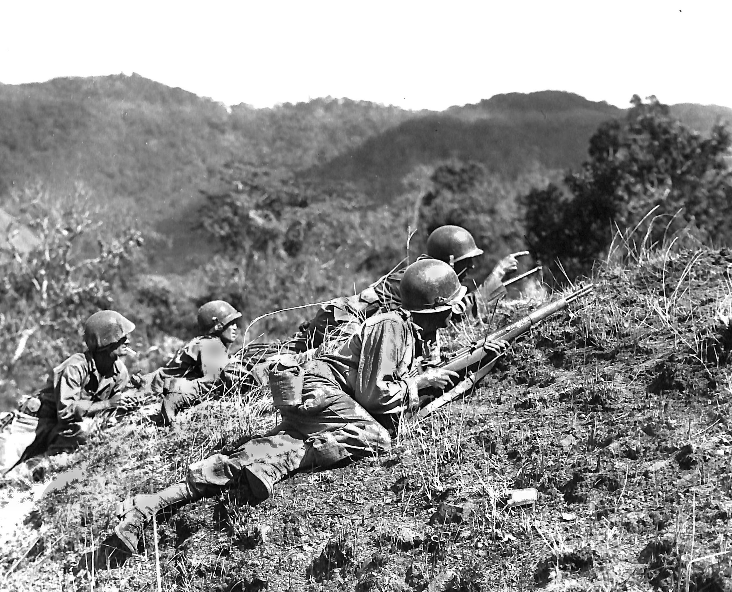 A squad leader points out a suspected Japanese position on Luzon in 1945 from behind a jagged ridge at the Balete Pass—guarded by cave defenses and hidden bunkers.