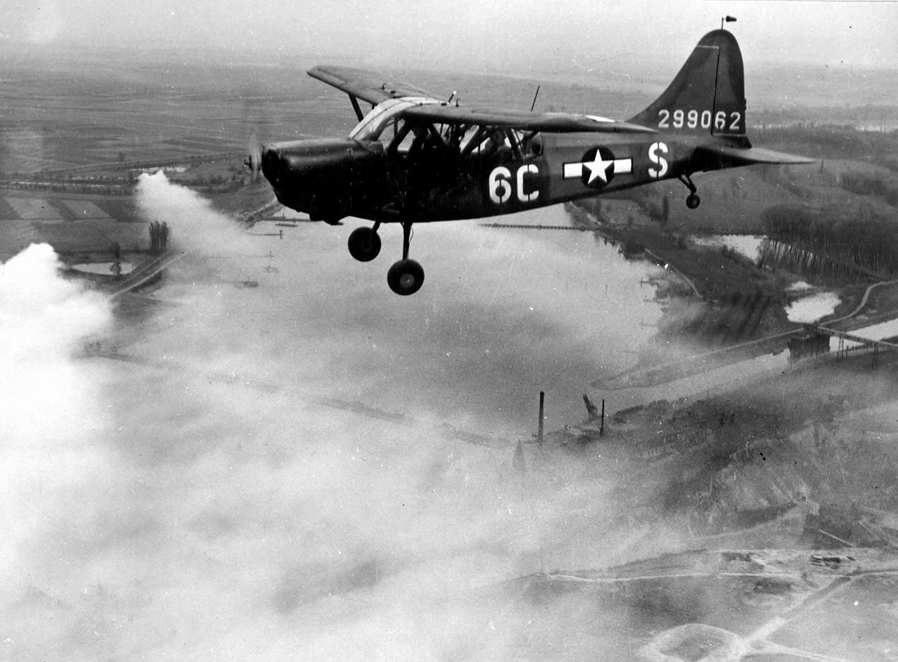 The pilot of an L-5 Sentinel aircraft directs fighter planes to targets on the far shore.