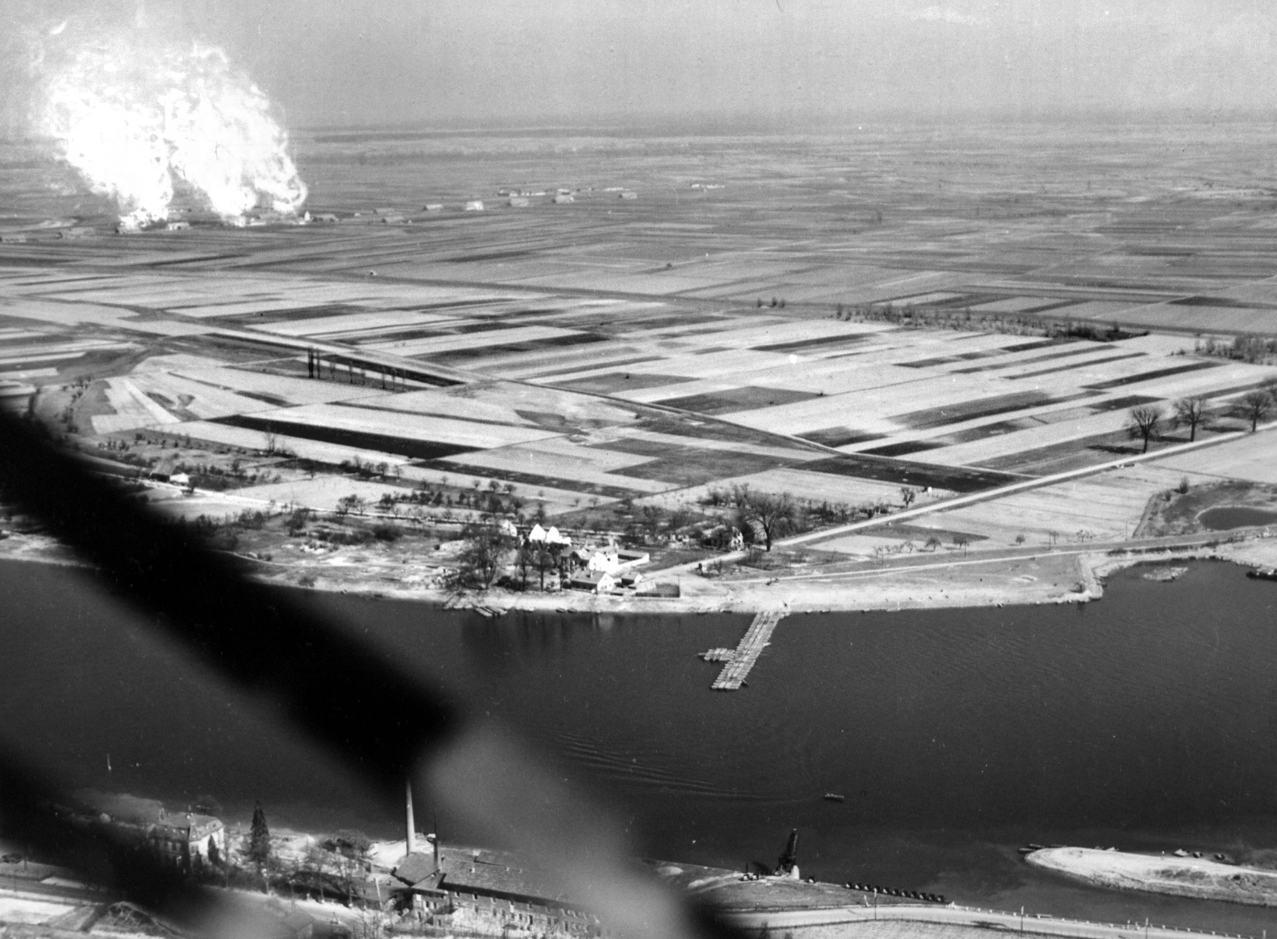Burning buildings (upper left) mark the progress of Patton’s Third Army as a bridge stretches across the Rhine River.