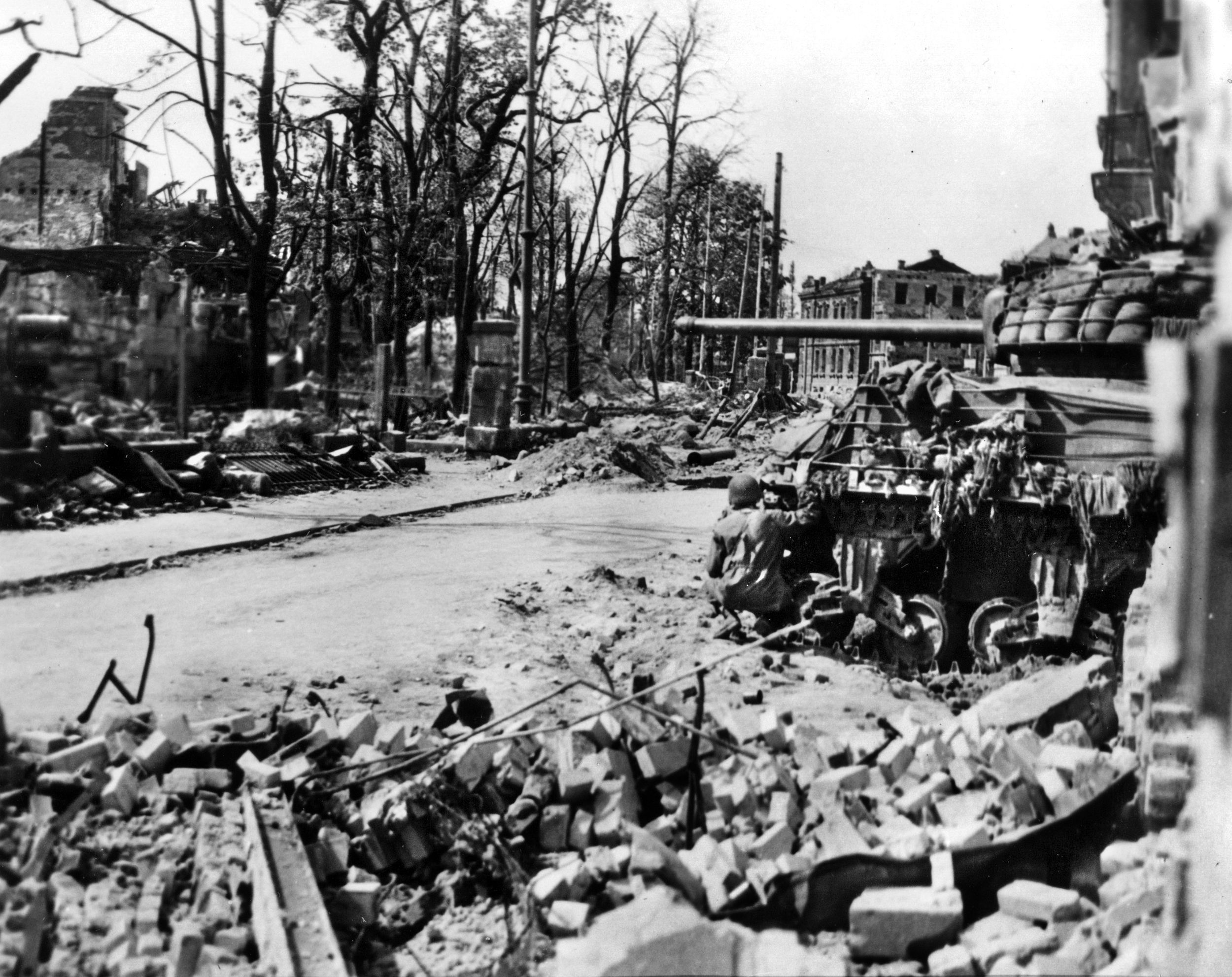 Under heavy enemy fire a soldier from the 3rd Division takes cover behind a Sherman tank in the ruins of Nuremberg on April 19, 1945. On the penultimate day of the battle, American armor provided essential mobile fire support, suppressing sniper nests and Panzerfaust teams as infantrymen cleared the city block-by-block.