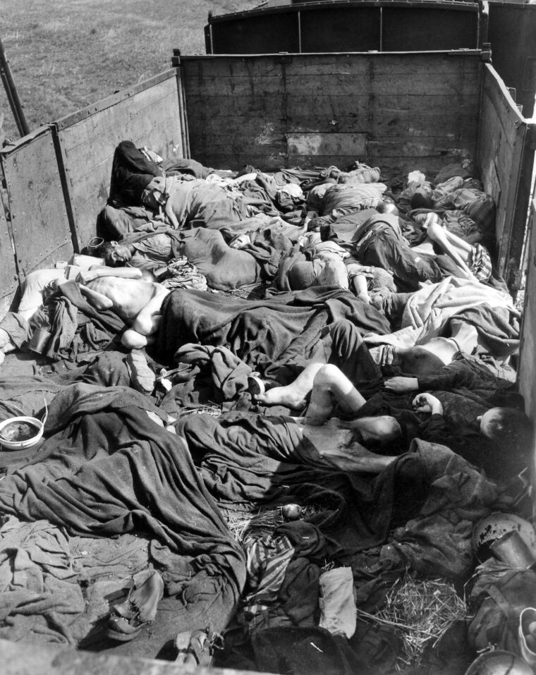 The bodies of hundreds of prisoners—with estimates ranging from 2,300 to more than 2,500—fill open freight cars of the Nazi “death train” at the rail siding outside the Dachau concentration camp on April 29, 1945. Evacuated from Buchenwald nearly three weeks earlier, many died from starvation and dehydration during the journey across Germany, while others were executed by SS guards en route. Amid the devastating horror, liberating U.S. troops discovered at least one survivor clinging to life among the corpses.