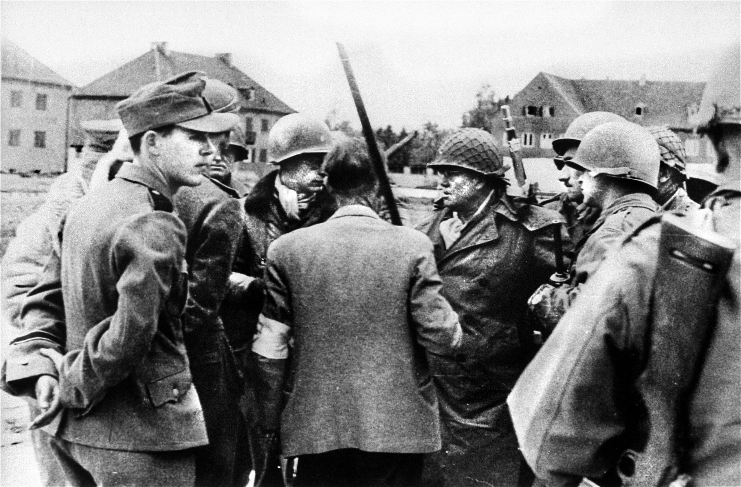 Brigadier General Henning Linden (center-right), assistant division commander of the 42nd “Rainbow” Infantry Division, confers with members of the surrender delegation outside the Dachau concentration camp on April 29, 1945. Pictured from left are an aide to SS-Obersturmführer Heinrich Wicker; Paul M. G. Levy, a Belgian journalist acting as an interpreter; and Dr. Victor Maurer of the International Committee of the Red Cross (back to camera), who arranged the terms of surrender and holds an improvised white flag attached to a broomstick. Flanking Linden are members of his U.S. Army bodyguard as details for the camp’s handover are finalized.