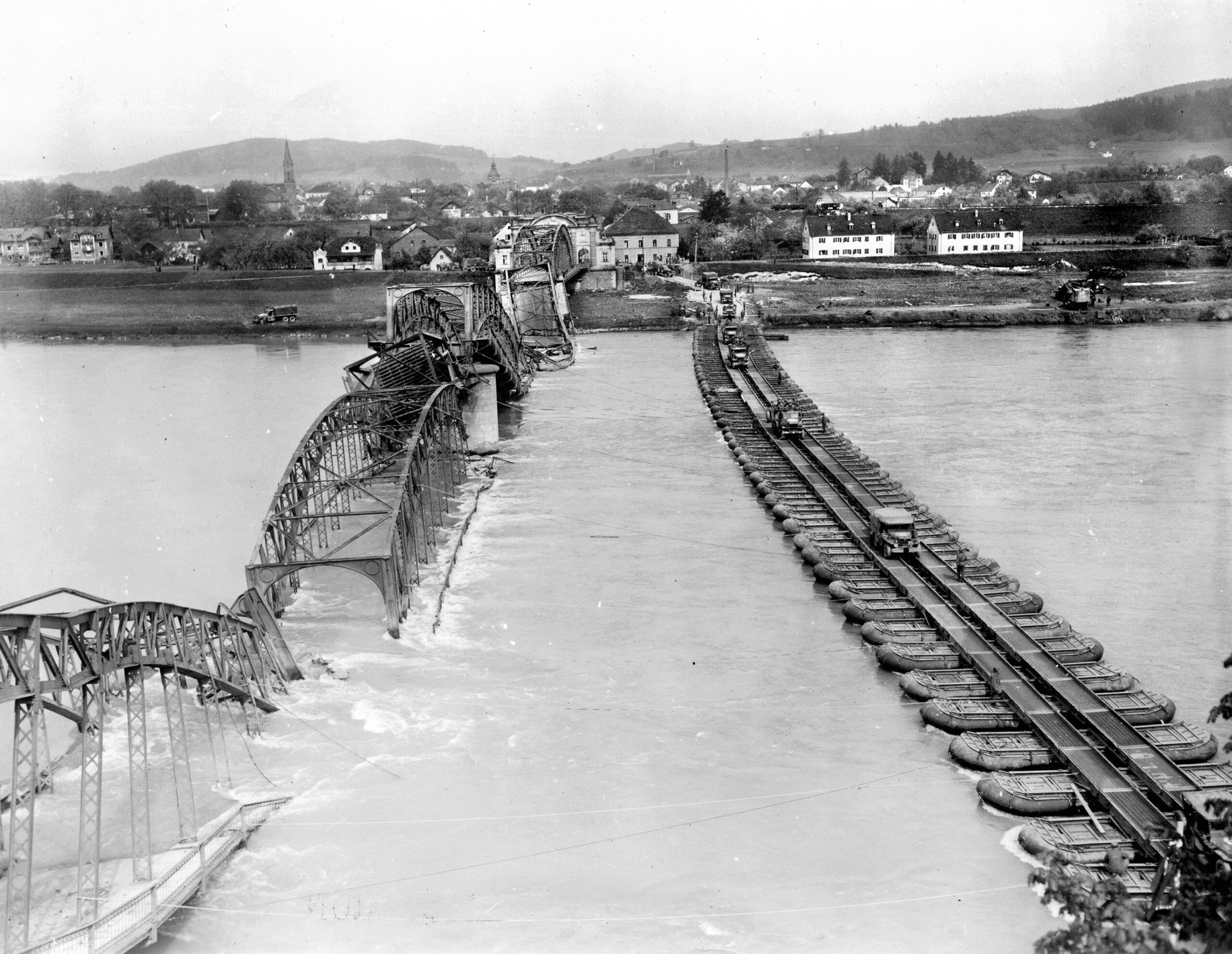 Reinforcements flow across the Inn River as American jeeps and trucks, stuffed with infantry, cross from Simbach, Germany, into Braunau, Austria. With the water barrier breached, these incoming forces moved swiftly to secure the sector and support ongoing operations in the closing days of the conflict.