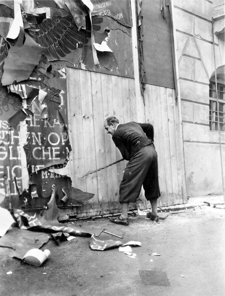 A citizen of Braunau am Inn removes a Nazi sign shortly after American forces occupied the city in early May 1945. For many local residents, the arrival of U.S. troops brought overwhelming relief—marking an end to the war and sparing the region from Soviet occupation. Despite its notoriety as Adolf Hitler’s birthplace, few in Braunau mourned his death.