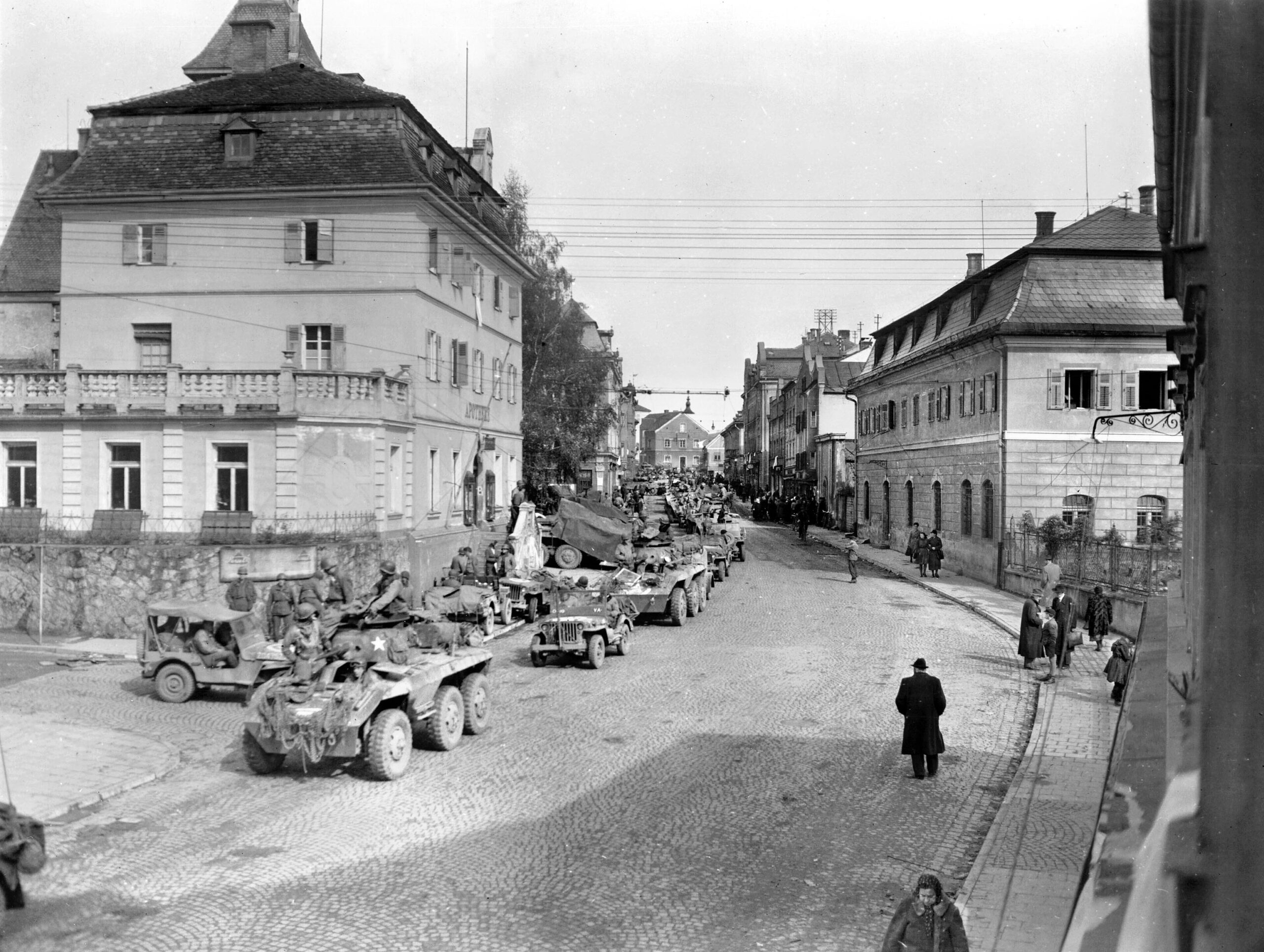 Two days after the 13th Armored Division secured Braunau, Austria, scout cars and jeeps of the 80th Infantry Division choked the streets of neighboring Simbach, Germany. Stretched in long queues along the riverbank, the vehicles waited their turn to rumble across the combat engineers’ pontoon bridge spanning the Inn River to join the final drive into the crumbling Reich.