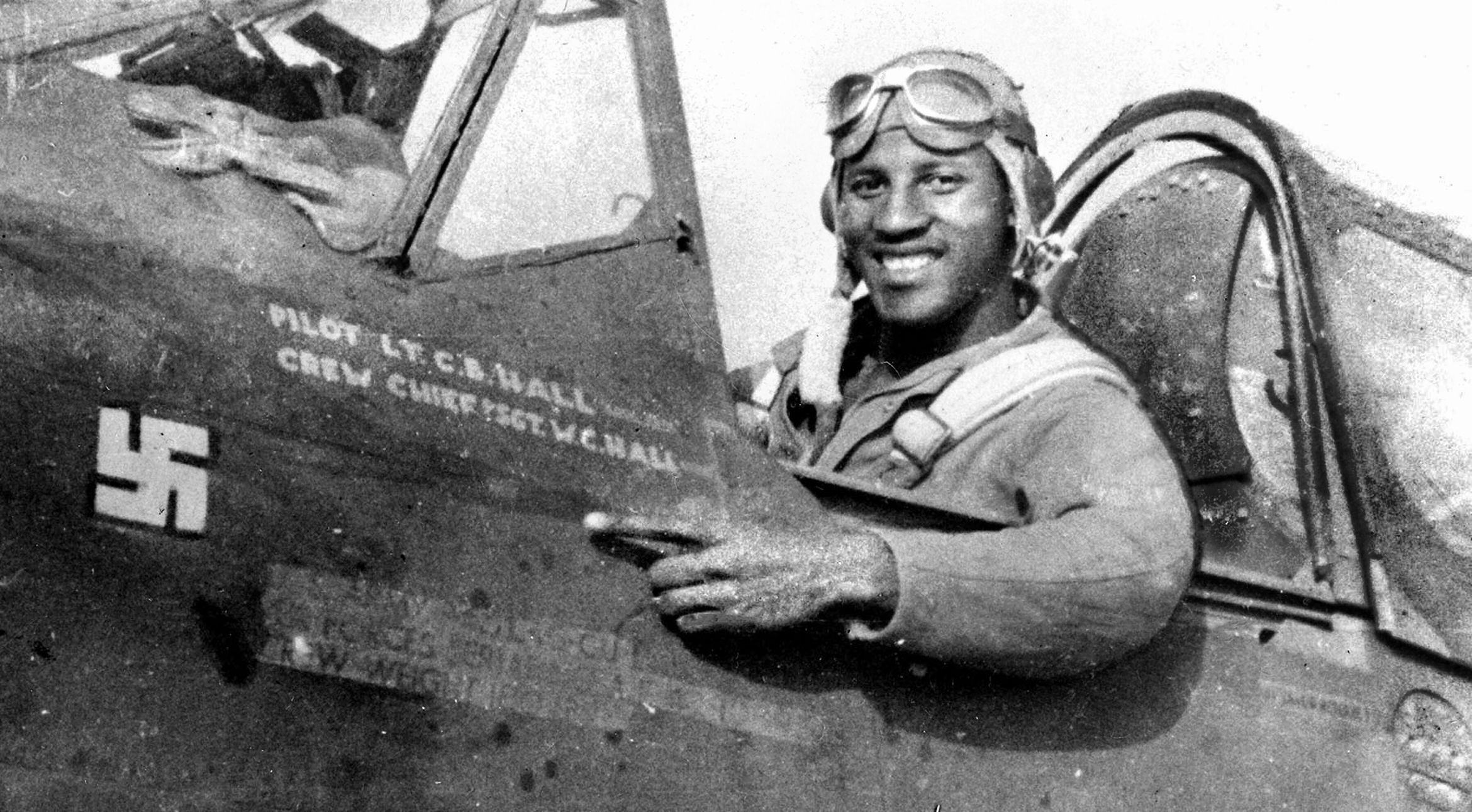 Lt. Charles B. Hall points to the newly painted swastika on his P-40 Warhawk, commemorating his July 2, 1943 victory over a German Focke-Wulf Fw 190. Unusually large, the victory emblem prompted fellow pilots to joke that friendly fighters might mistake Hall’s plane for an enemy aircraft.