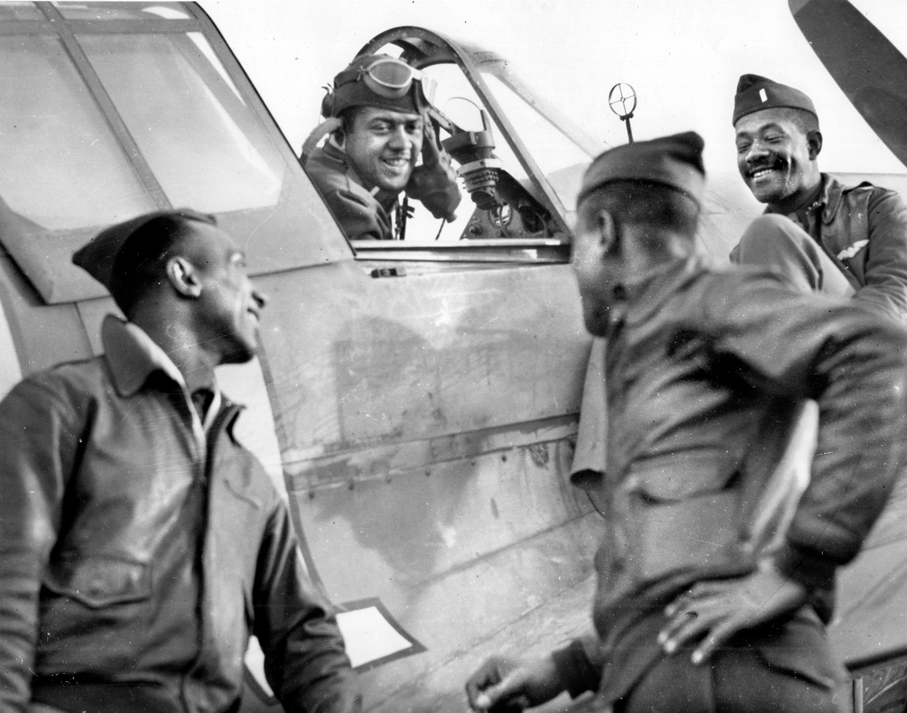 Pilots of the 99th Fighter Squadron gather around a P-40 Warhawk in North Africa: Lt. W. V. Eagleson in the cockpit, flanked by Capt. Lemuel R. Curtis (left), Lt. Charles B. Hall (center), and Lt. Willie Ashley (right).