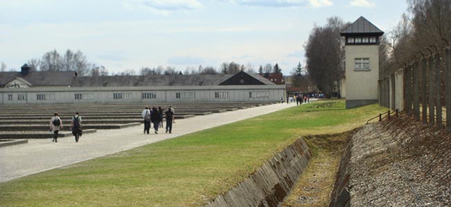 Footprints of the barracks (left), a partially filled in moat, sinister guard tower, and barbed-wire fence silently remind visitors of the cheapness of life at Dachau. 