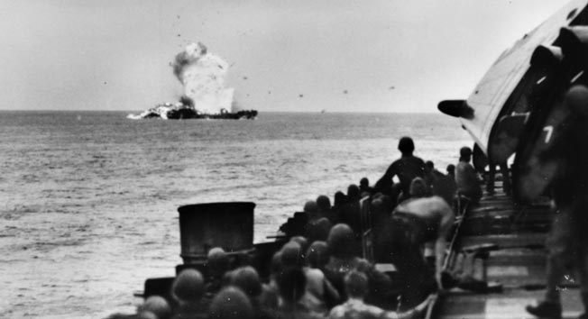 Men aboard the escort carrier USS Tulagi watch as a kamikaze strikes LST-447 near Okinawa, April 6, 1945. Fortunately, the LST was empty when attacked. BELOW: The Essex-class carrier USS Hancock burns after being struck by a Japanese suicide plane off Okinawa, April 7, 1945. A TBM Avenger is visible above the ship (arrow). The ship survived. 