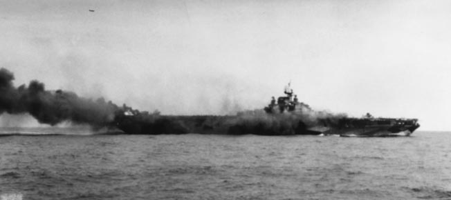 The Essex-class carrier USS Hancock burns after being struck by a Japanese suicide plane off Okinawa, April 7, 1945. A TBM Avenger is visible above the ship (arrow). The ship survived. 