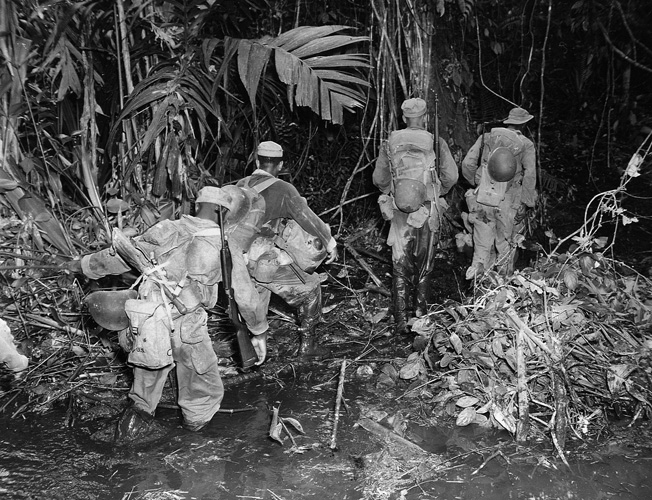 The hot, humid jungle conditions on Bougainville made combat an exhausting, harrowing experience for all troops. Here a patrol from the 25th Regiment slogs along a muddy, enemy-infested trail to reach their objective.