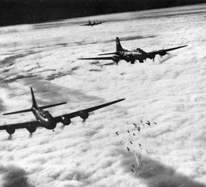American Boeing B-17F Flying Fortress heavy bombers drop their bombloads through thick cloud cover against an unseen target below. 