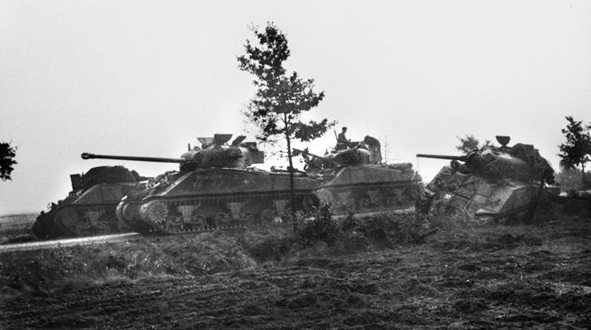 An up-gunned Sherman "Firefly" tank of the Irish Guards rolls past three other tanks knocked out during Operation Market-Garden on September 17, 1944.