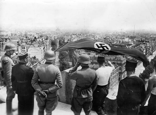 Standing atop the Arc de Triomphe in Paris, German soldiers and collaborationist French officials see to the raising of the swastika-emblazoned Nazi banner from one of the most recognizable symbols of French national pride. Paris endured four years of Nazi occupation before its liberation by the Allies in August 1944.