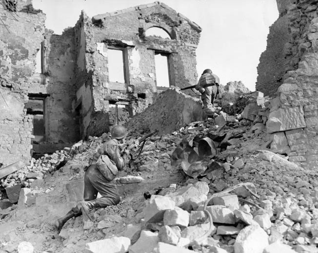 Members of an American engineer unit scramble over piles of rubble during the advance into Brittany, August 1944. Many French cities were destroyed or badly damaged during the fighting.