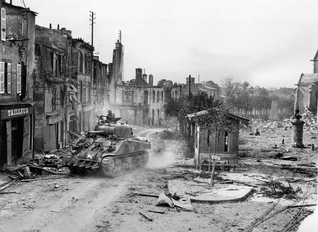 A Sherman tank equipped with a “hedge-buster” welded to its front hull advances through the deserted streets of Lambezellic en route to Brest, August 1944. 