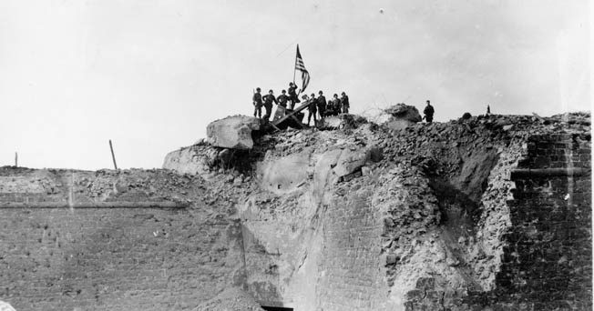 After the Citadel at St. Malo fell, GIs raise the American flag over an antiaircraft position atop the rubble, August 26, 1944.