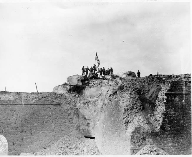 After the Citadel at St. Malo fell, GIs raise the American flag over an antiaircraft position atop the rubble, August 26, 1944.
