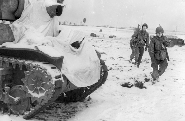 Three “Screaming Eagle” paratroopers pass a U.S. 75mm howitzer motor carriage that has been snow-camouflaged with white sheets. Once Lt. Gen. George S. Patton’s Third Army reached Bastogne, Buford and his comrades received armor support.