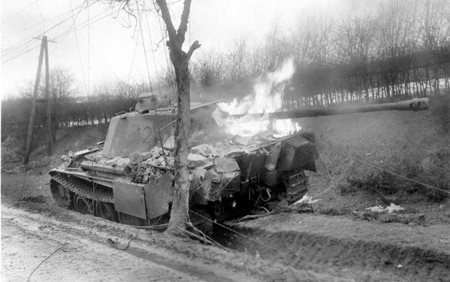 A German PzKpfw. V Panther medium tank, its long-barreled 75mm main gun jutting from the tur- ret, blazes after being knocked out in combat in the vicinity of Bastogne, the vital Belgian crossroads town that played a pivotal role in the Battle of the Bulge.