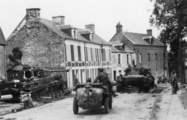 A PzKpfw IV “634” of the Panzer Lehr (far left) has an optimal view of the Villers-Bocage street from its vantage point behind a house.