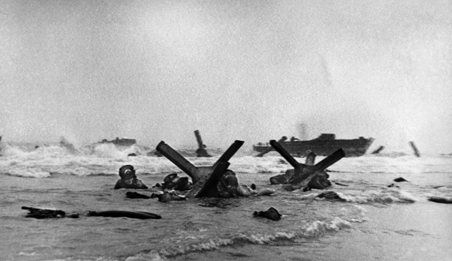 In this famous photo of the D-Day landings on Omaha Beach, American infantrymen of the 16th Regiment, 1st Division seek shelter from German mortar and small-arms fire behind a hedgehog beach obstacle. The helmet with the white arc worn by the man at far left indicates he is an army combat engineer.