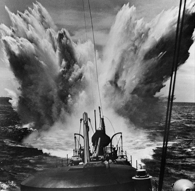 A depth charge sends a plume of water skyward as it detonates off the fantail of a destroyer in the Atlantic Ocean. 