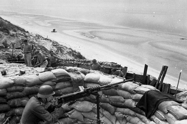 While his shirtless comrades improve their coastal defense position, a German soldier manning an obsolescent French-made Hotchkiss M1914 8mm machine gun has a commanding view of the beach near Dieppe.