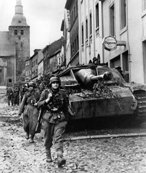 German panzergrenadiers accompanied by a Sturmgeschutz IV assault gun mounting a 75mm main weapon advance through the rubble strewn streets of the city of Aachen. 