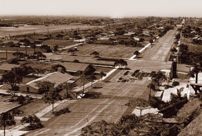 This excellent overview of the camouflaged Douglas factory in Santa Monica shows how detailed and realistic the false rooftop neighborhoods were. In addition to tree-lined streets and buildings of varying shapes and sizes, there were sidewalks, detached garages, and empty lots. Note the sizable, but unplanned, “potholes”—actually rips in the cammo netting, in the center. By the time this picture was taken in 1945, such potholes were no longer being repaired. The Clover Field flightline is visible in the upper left. 