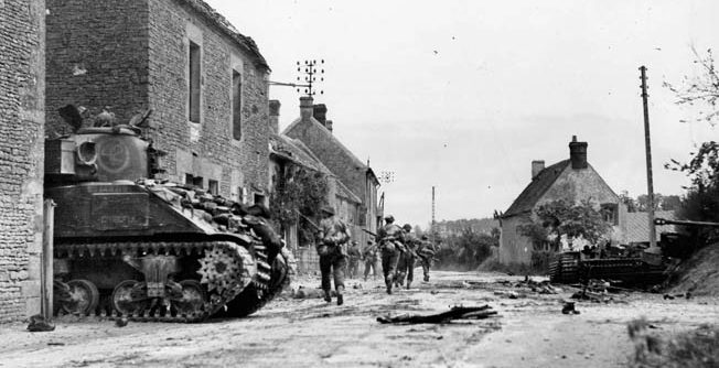 Canadian troops, accompanied by a Sherman/Grizzly tank, depart St. Lambert-sur-Dives. The “Corridor of Death” is less than a mile up ahead.