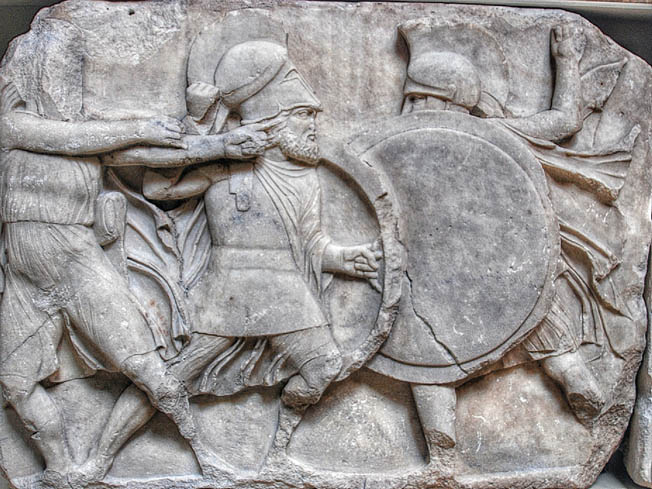 A Greek hoplite is shown locked in combat with a foe in a period sculpture. Hoplite tactics included othismos, which called for the front line to push the enemy back with their shields. 